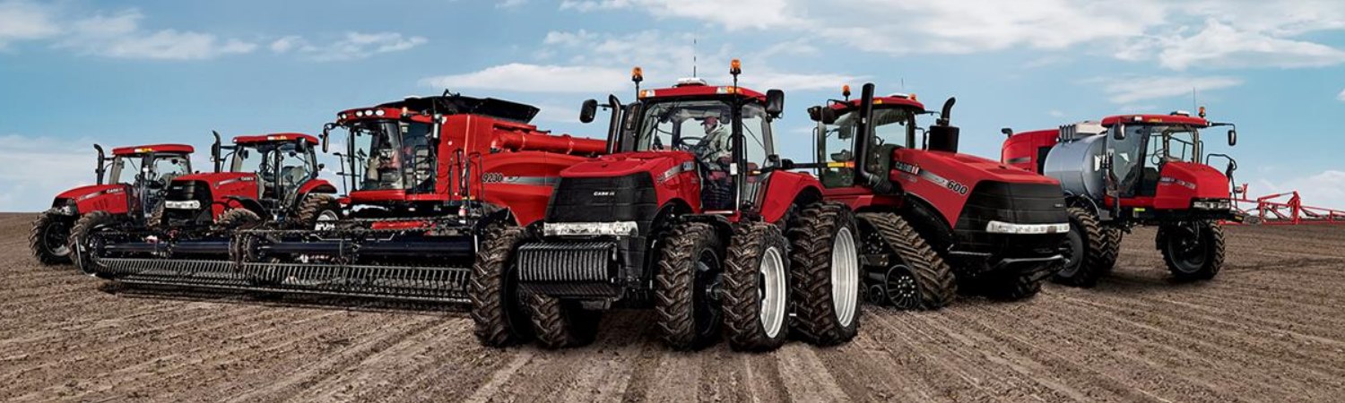 Various models of Case IH tractors lined up in a row on sunny dirt field.