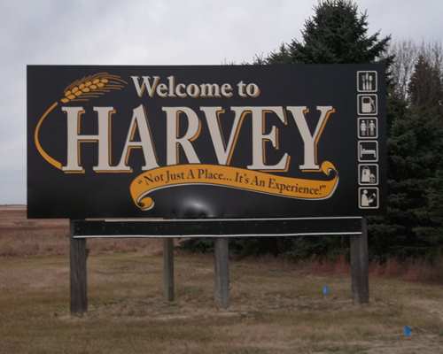 Black billboard sign that says "Welcome to Harvey, Not Just a Place.... It's an Experience"