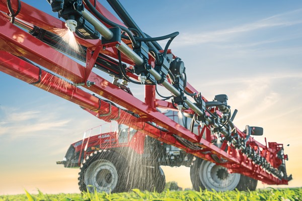 Red tractor with spraying apparatus hosing down green field.