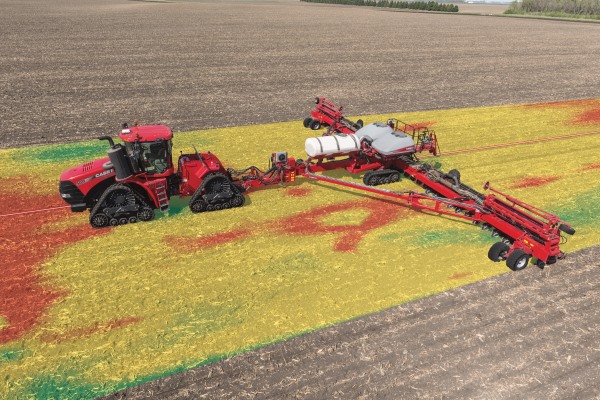 Red tractor with spraying apparatus hosing down dirt field.