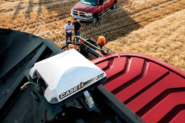 Roof housing of red tractor in golden field with two men juxtaposed between tractor and red truck.
